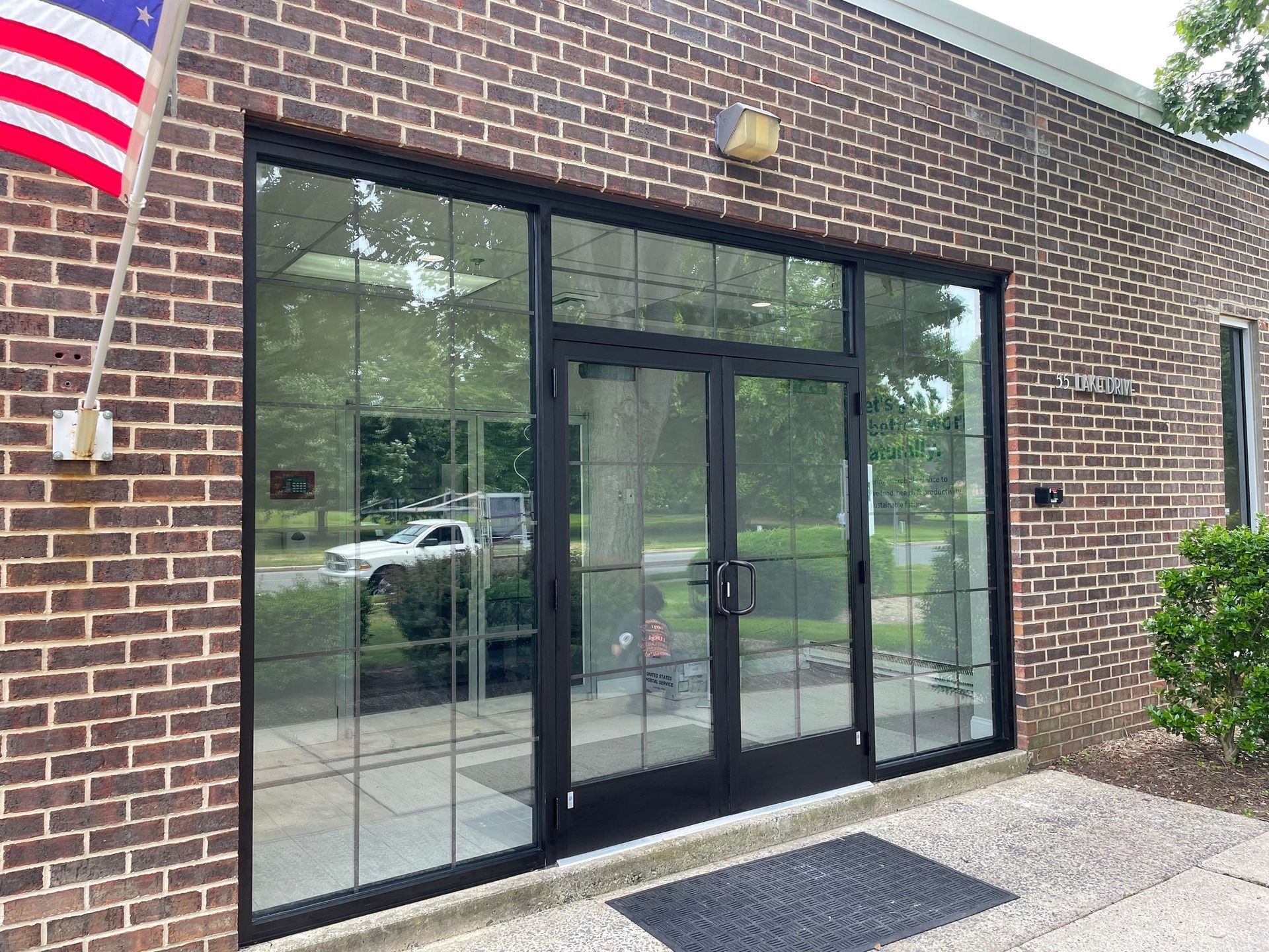 A brick building with a large glass door and an american flag hanging from the side.
