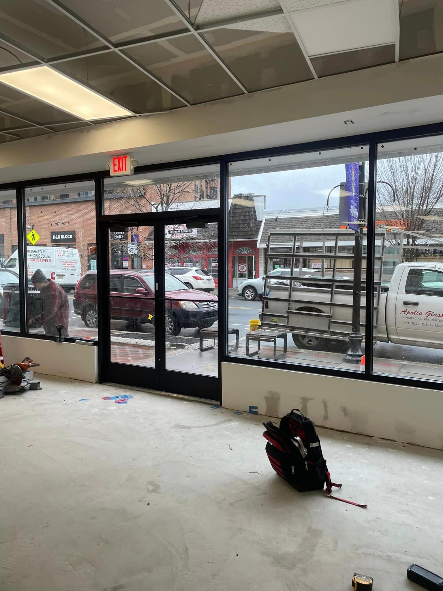 A large empty room with a lot of windows and a red exit sign.