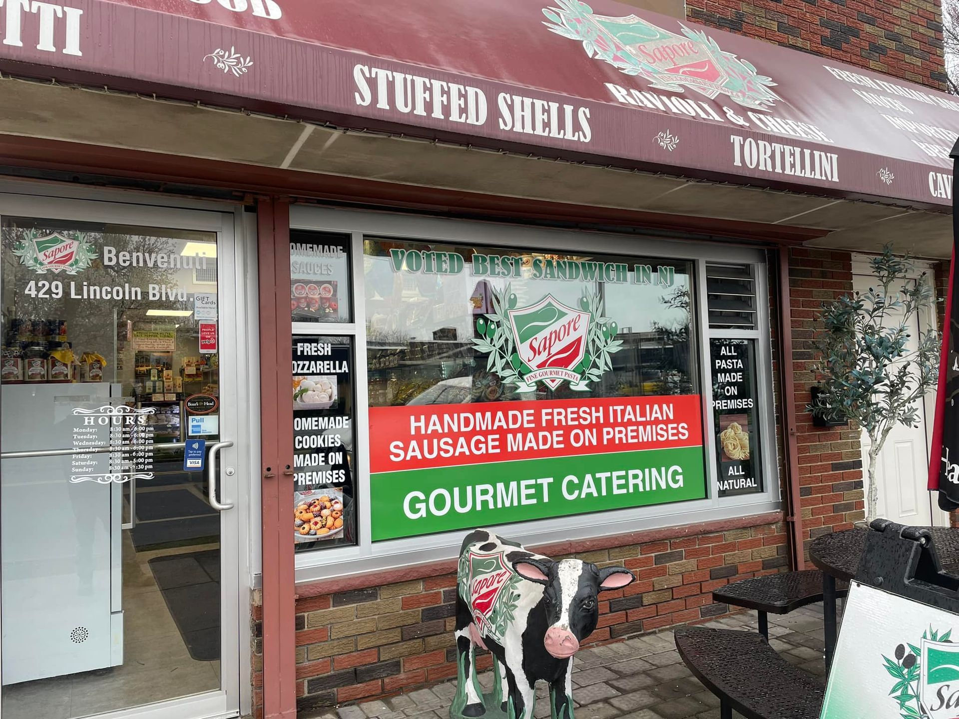 A cow is standing in front of a store that sells stuffed shells.