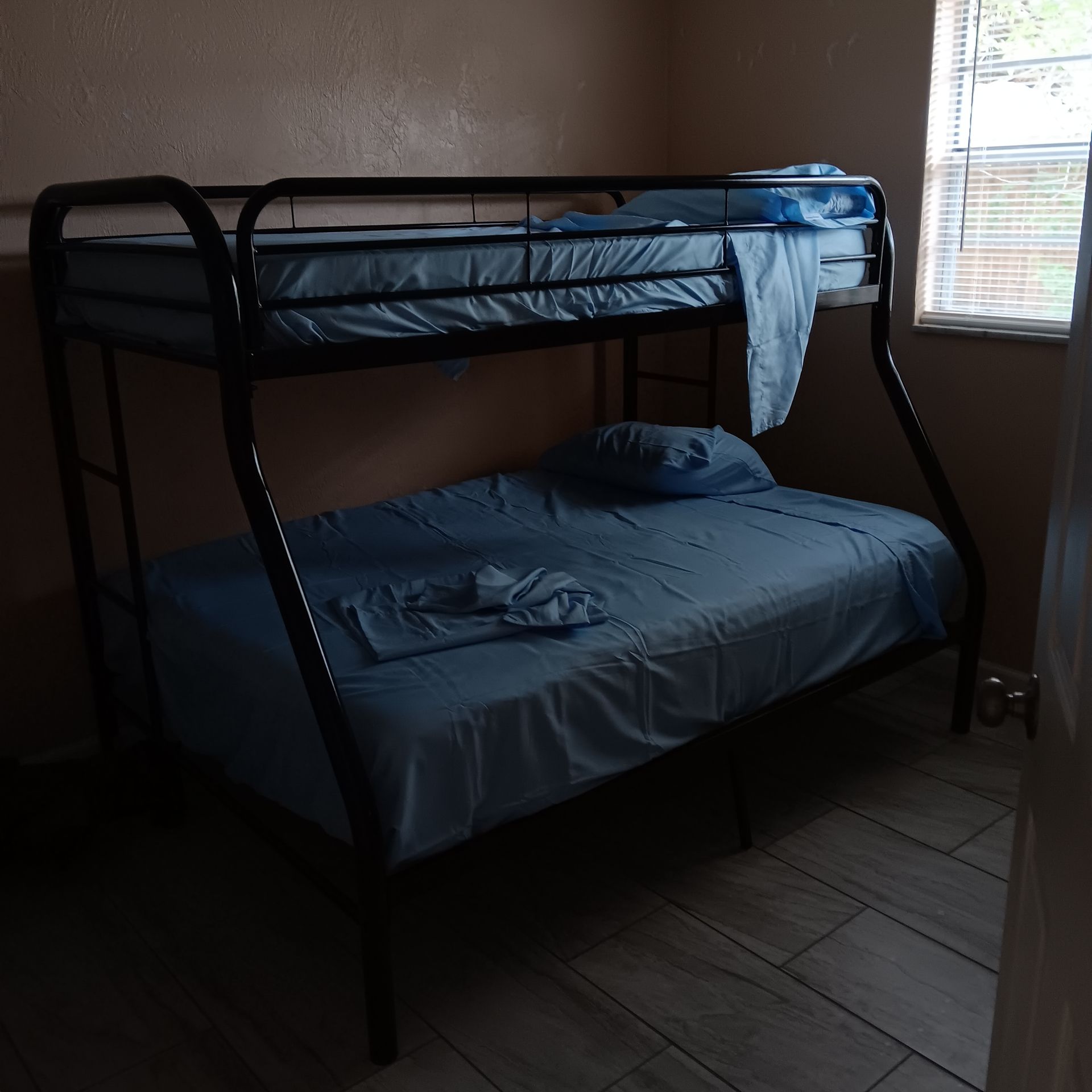 Black bunk beds with blue bedding in a room with a window and tiled floor.