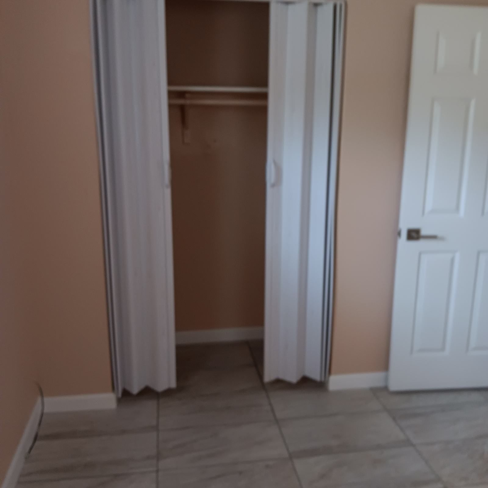 Closet with bi-fold doors open, a white door on the right, tan walls, and tile floor.