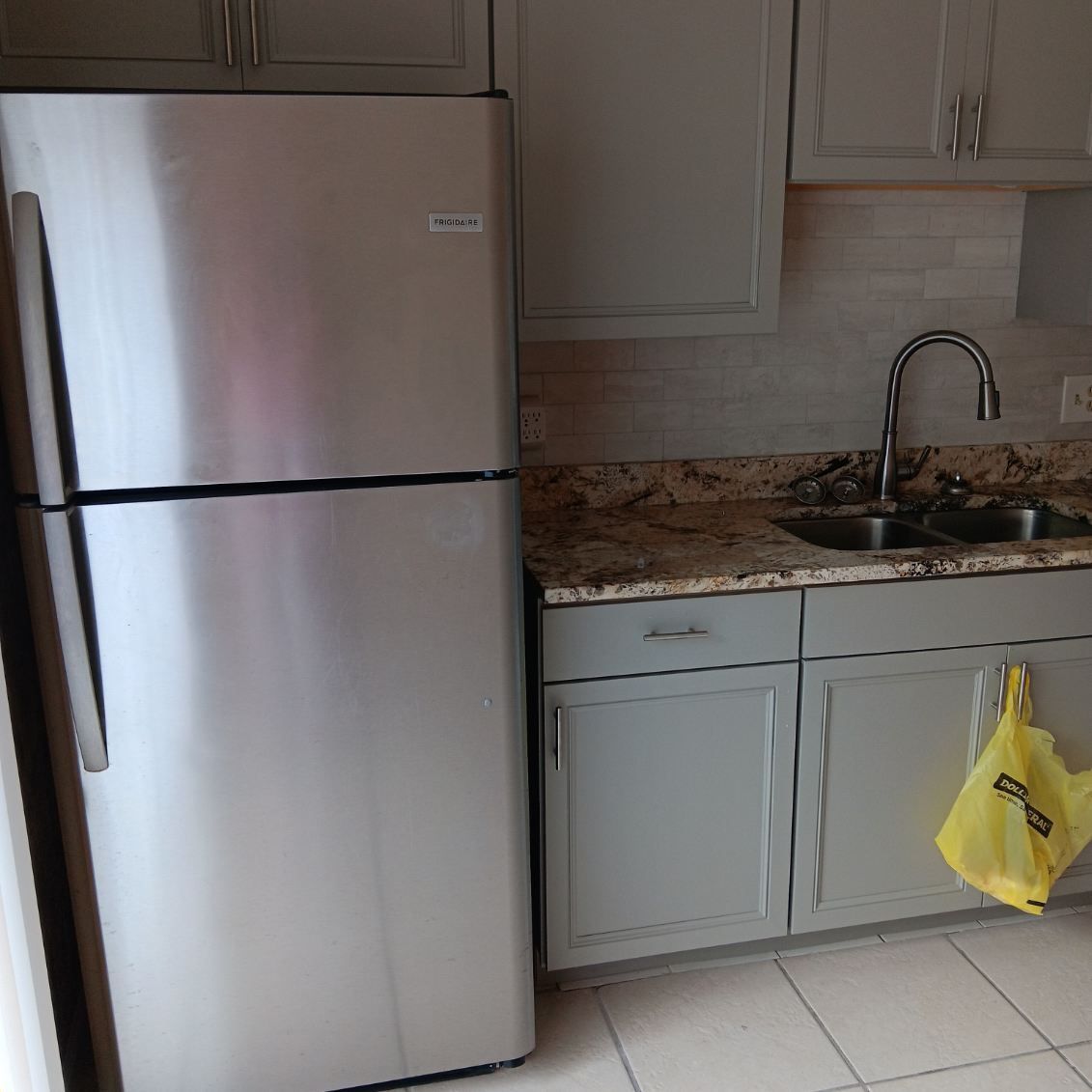 Stainless steel refrigerator next to a kitchen sink and cabinets painted gray.