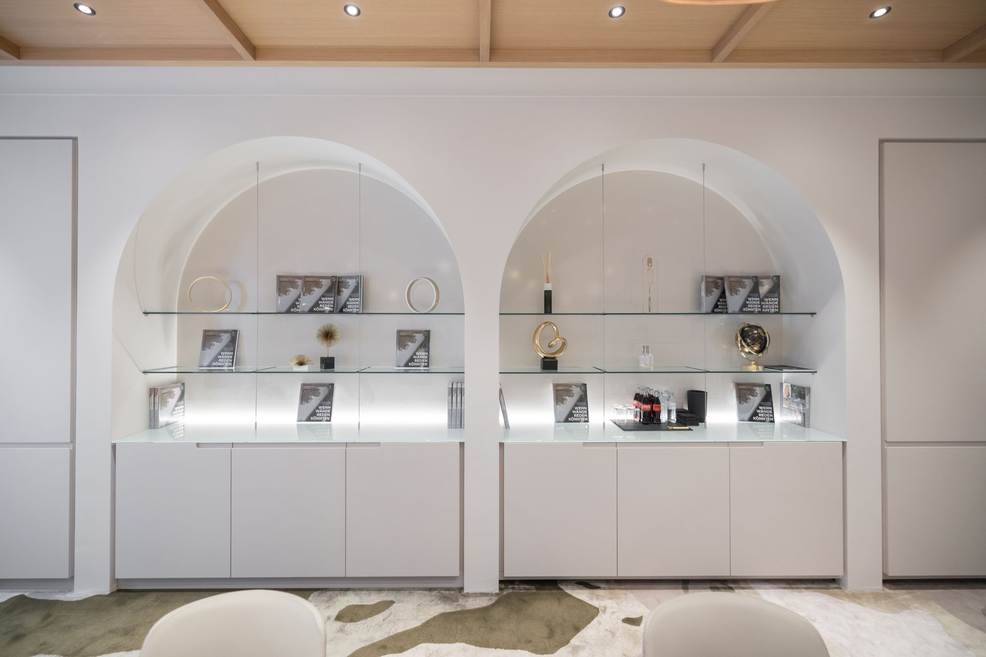 Zwei bogenförmige Wandvitrinen mit Glasregalen und Unterschränken, die dekorative Objekte und beleuchtete Hintergründe präsentieren.