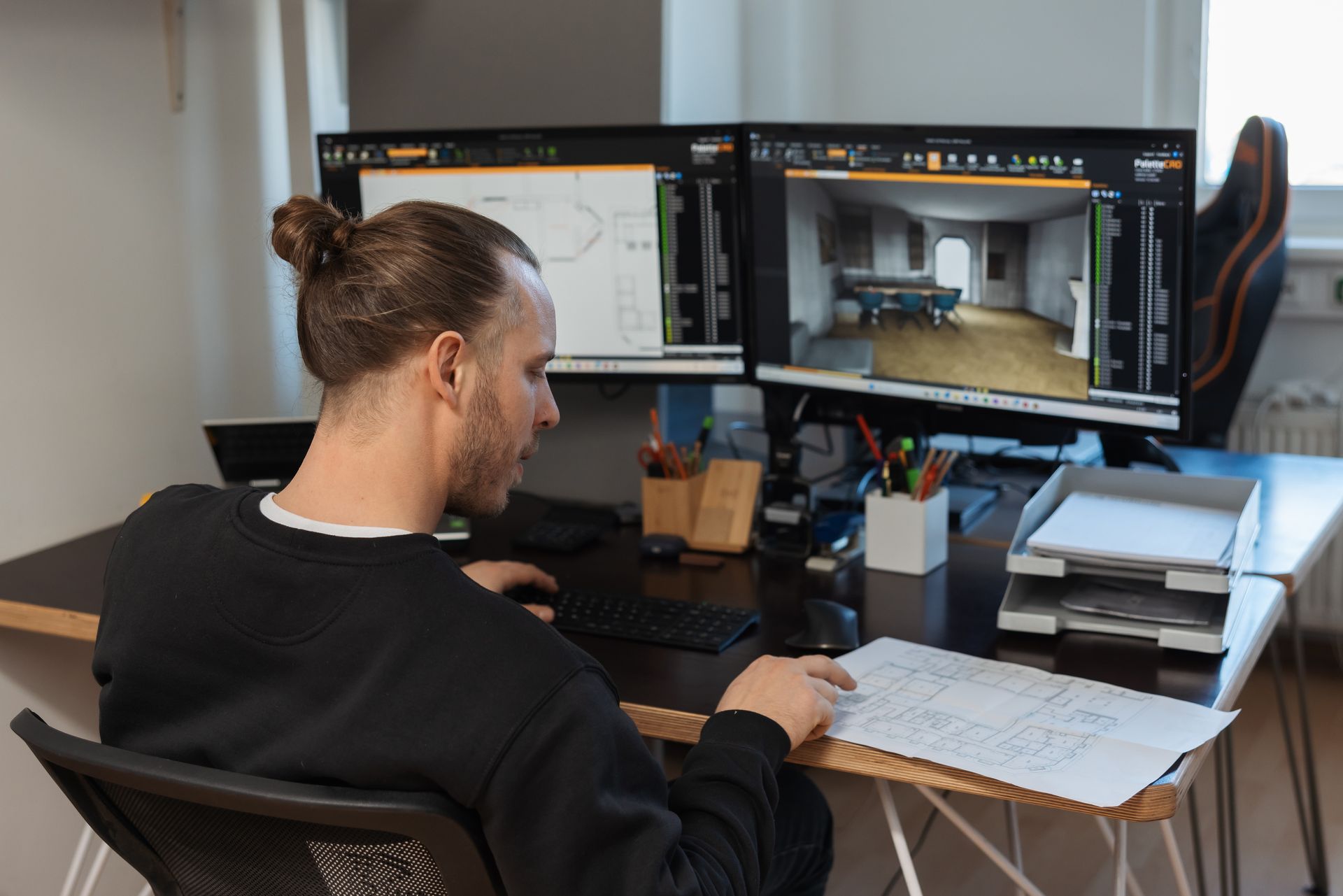Ein Mann sitzt an einem Schreibtisch vor zwei Computerbildschirmen.