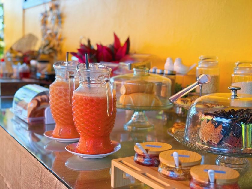 Mesa de buffet com jarras de vidro contendo bebidas cor-de-rosa, xícaras de chá, doces e um arranjo decorativo.