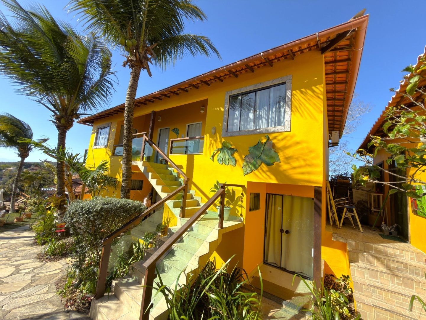 Vila tropical amarelo-vivo com escadas, palmeiras e um céu azul ensolarado.