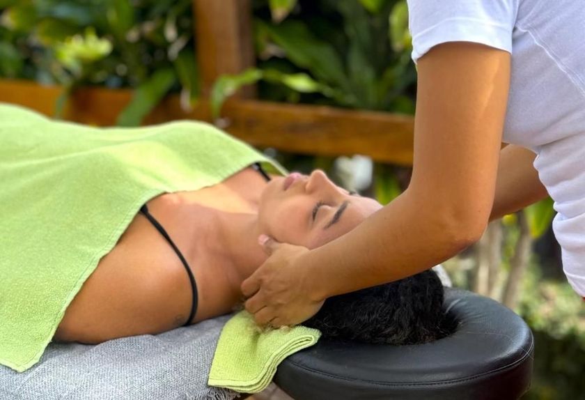 Mulher recebendo massagem no pescoço deitada em uma maca, coberta com uma toalha verde, em um spa.