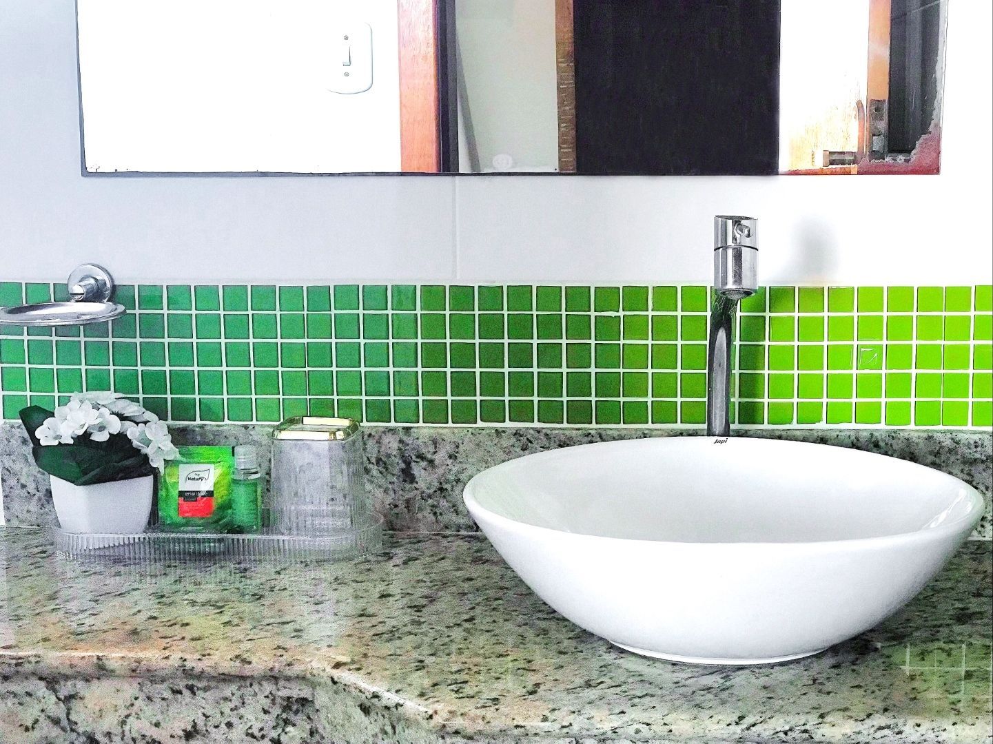 Pia de banheiro com cuba de apoio branca, torneira cromada e backsplash de azulejos verdes sobre bancada com detalhes em relevo.