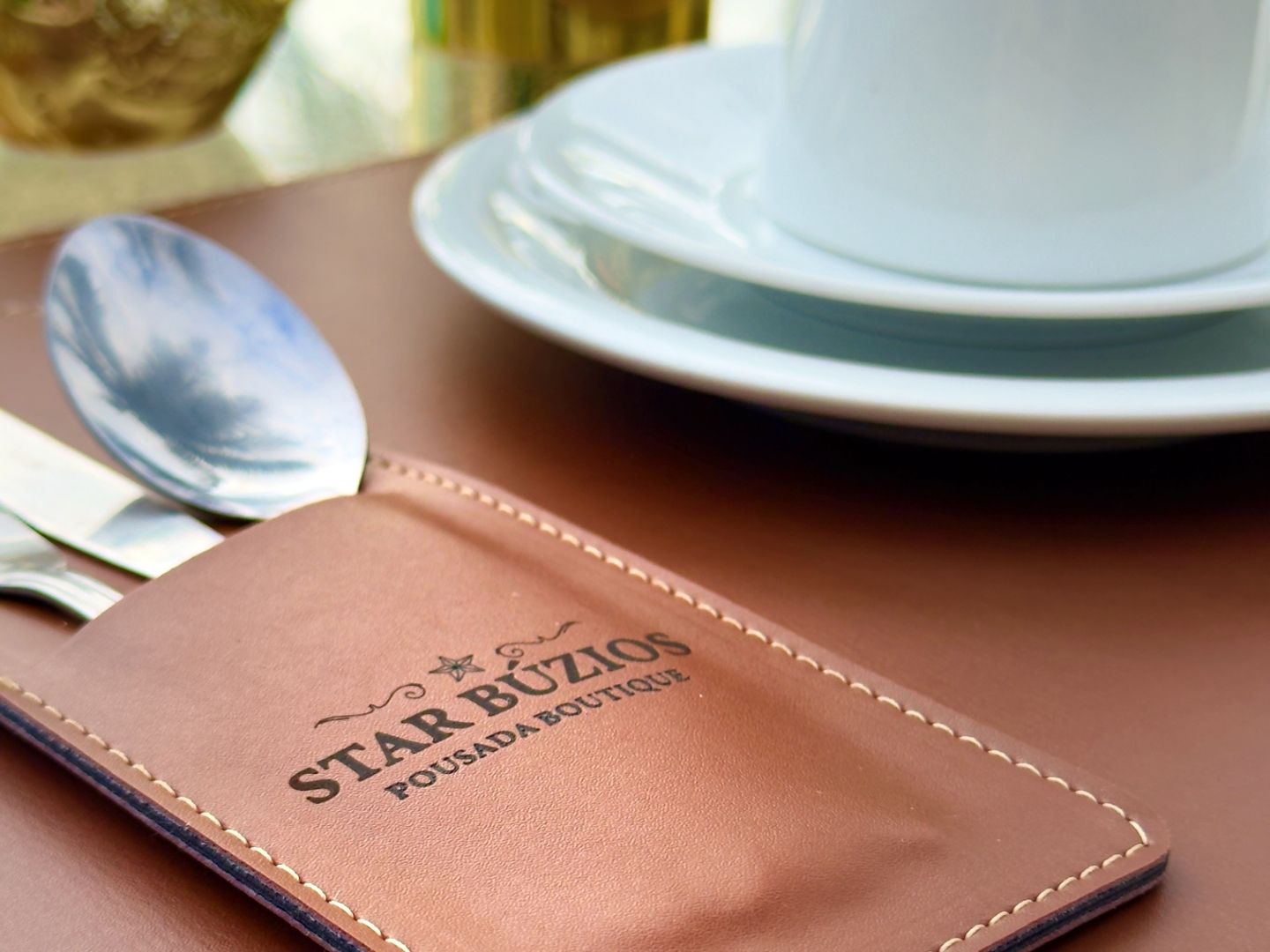 Carteira de couro sobre uma mesa de café ao lado de uma colher, um pires e uma xícara branca.