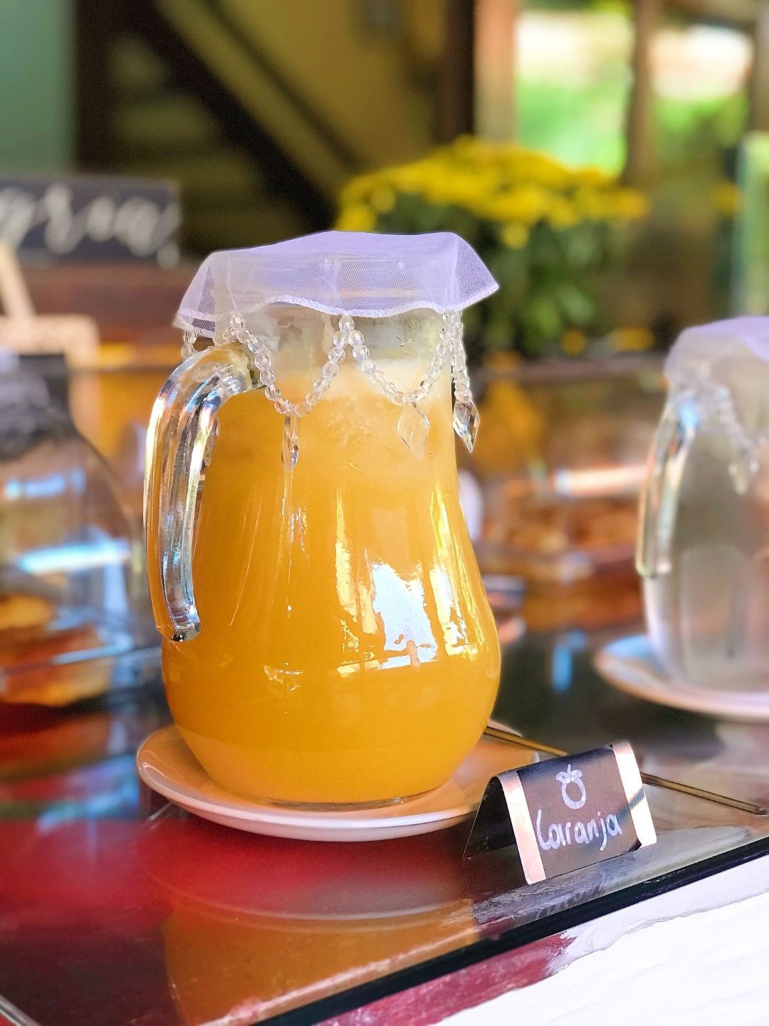 Jarra de suco de laranja com gelo e tampa branca sobre uma mesa de café.