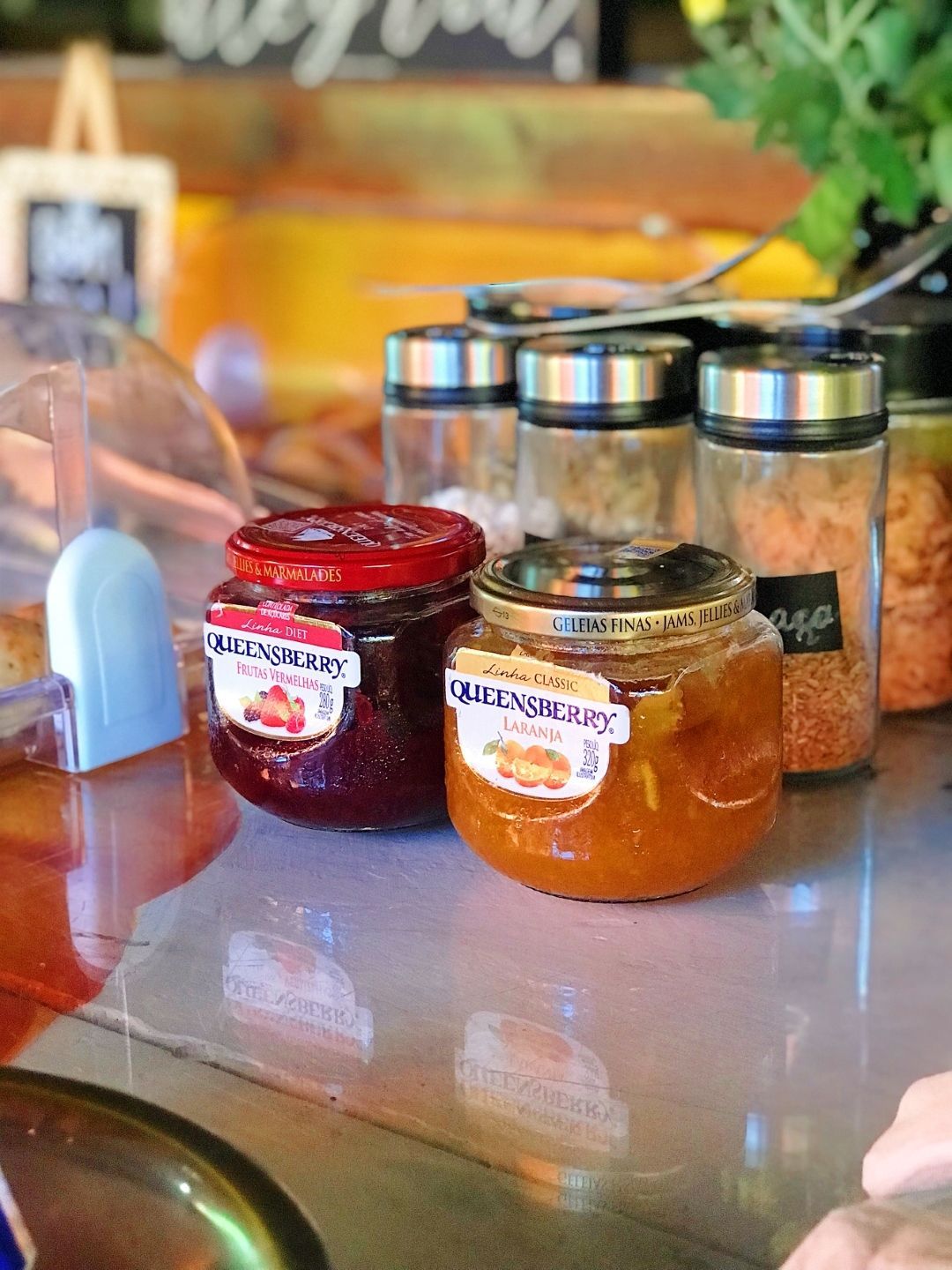Potes de geleia vermelha e laranja com tampas de metal em um balcão de café.