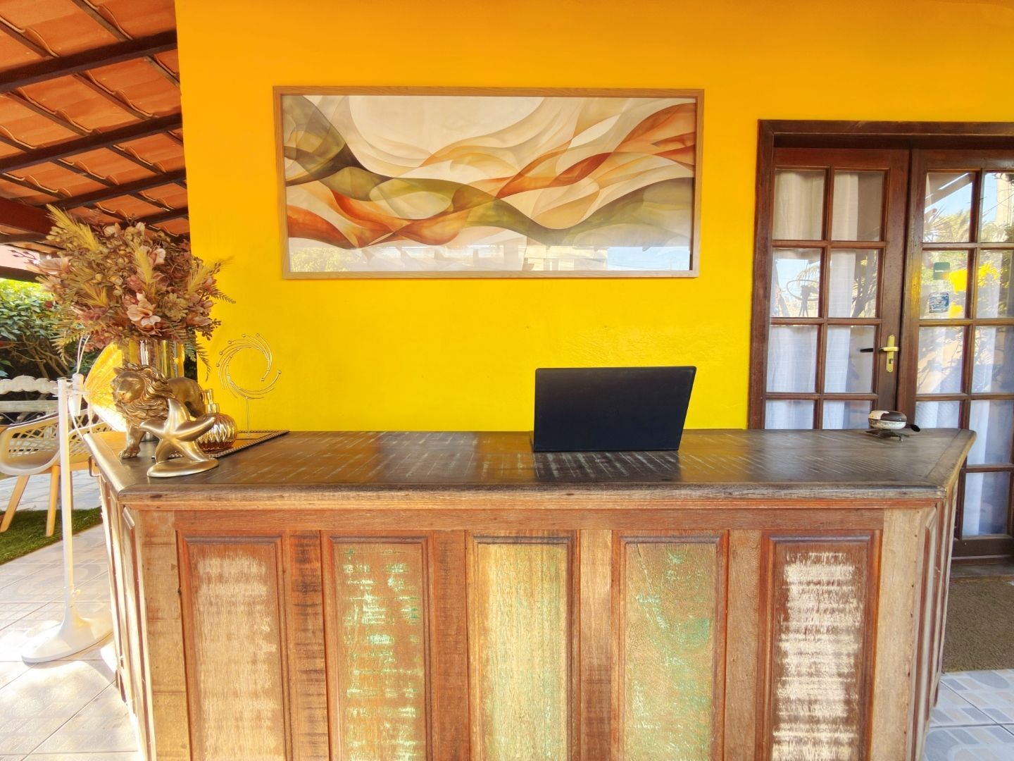 Balcão de recepção rústico contra uma parede amarela vibrante com um quadro emoldurado e portas de vidro.
