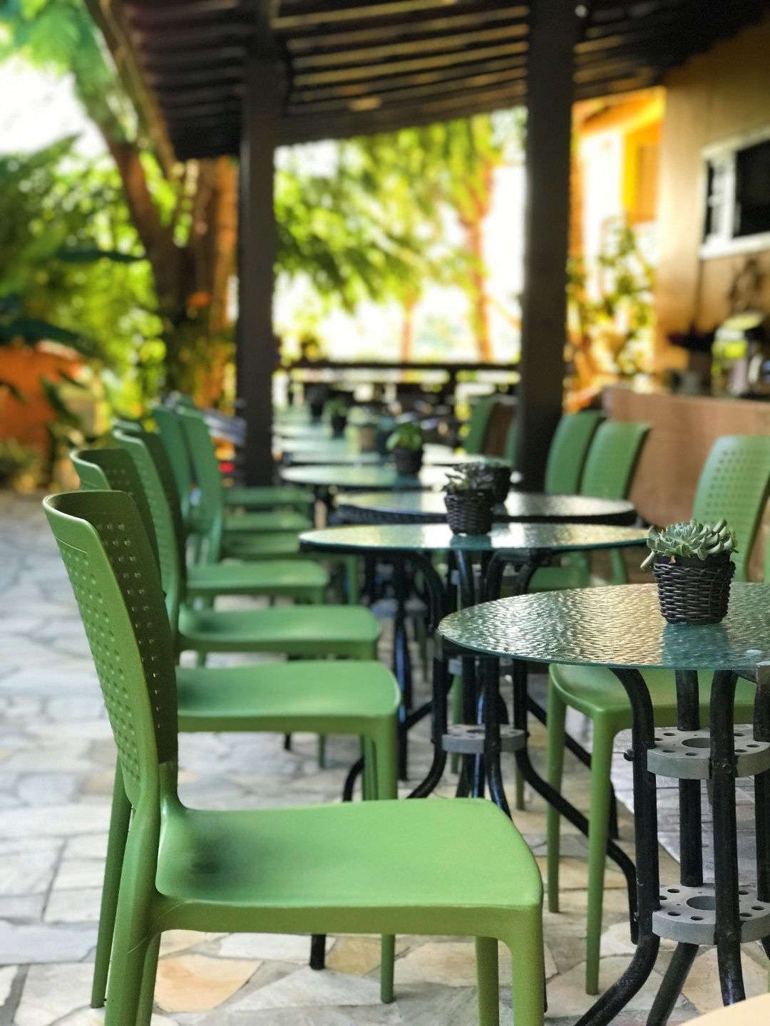 Cadeiras de pátio verdes e mesas pretas enfileiradas ao longo de uma passarela de um café ao ar livre.