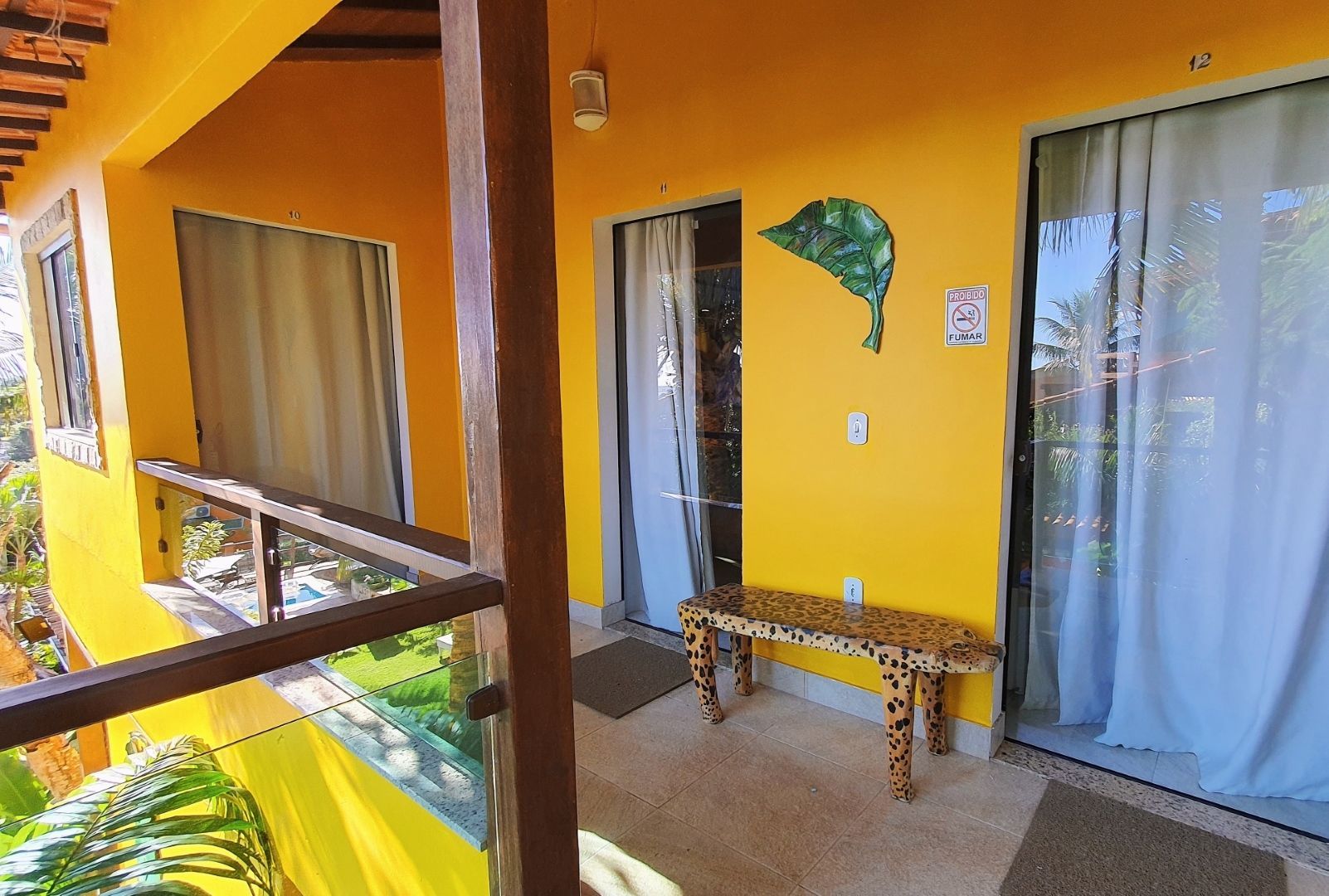 Varanda amarela com corrimão de madeira, banco e cortinas azuis do lado de fora de um quarto com a porta aberta.