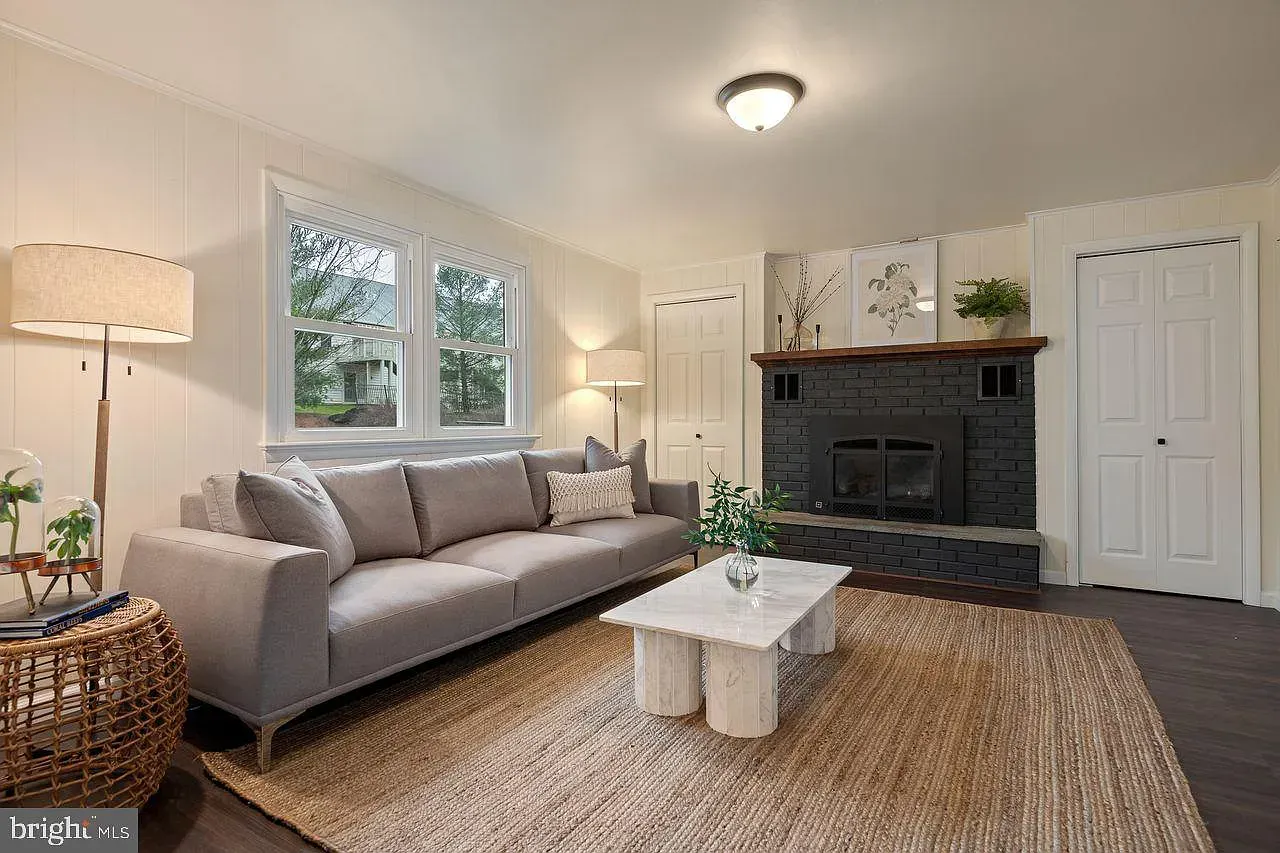 Bright living room with gray sofa, white coffee table, woven rug, fireplace, and large windows