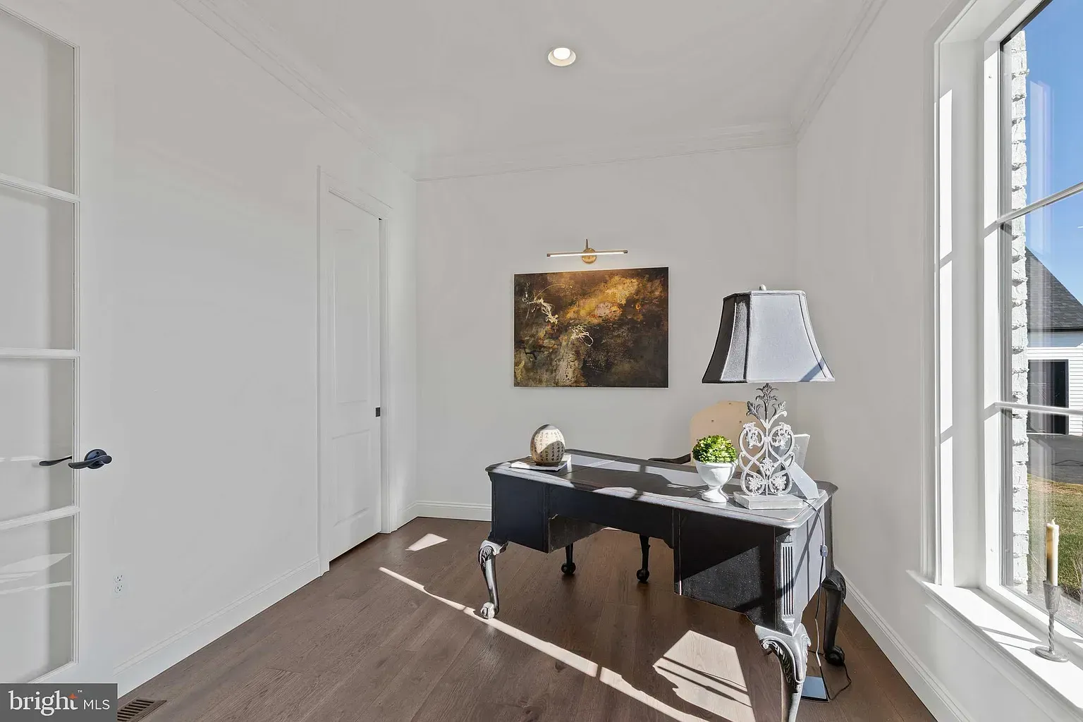 Bright home office with a black desk, lamp, wall art, and large window overlooking city buildings