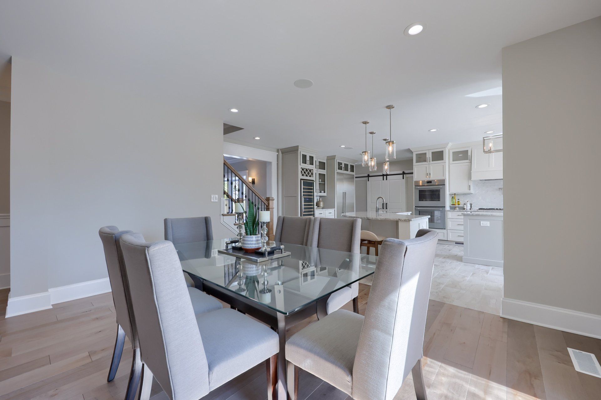Modern dining room with glass table, white chairs, and open kitchen in the background