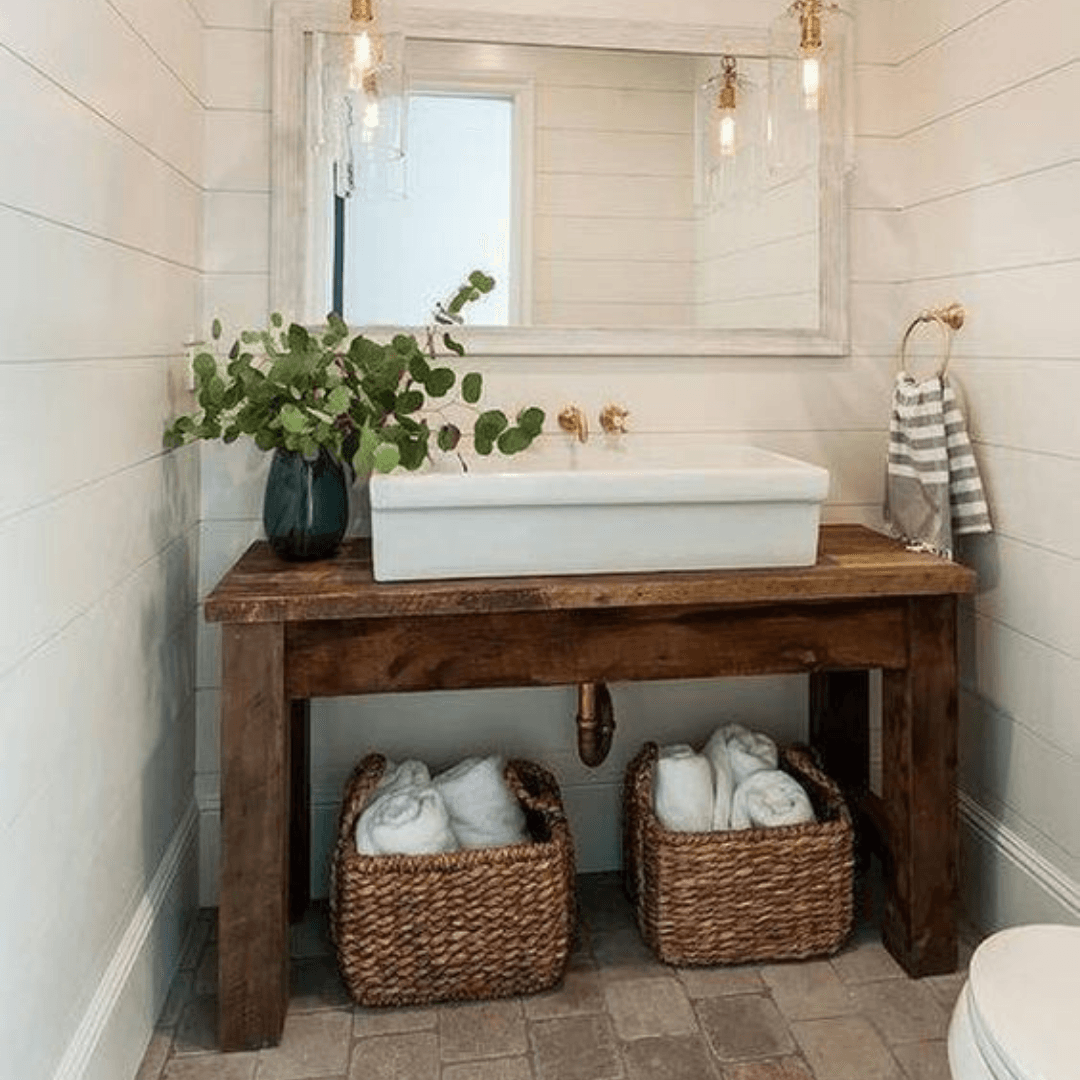Rustic bathroom vanity with white sink, mirror, greenery, and wicker baskets underneath