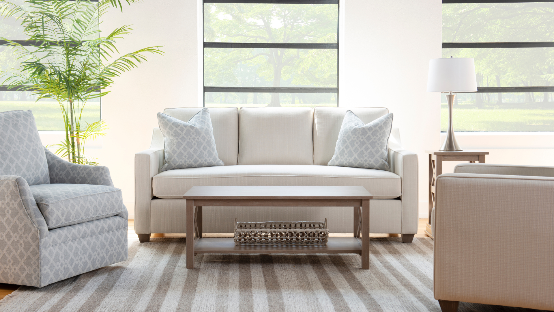 Bright living room with a beige sofa, armchair, coffee table, lamp, and large window