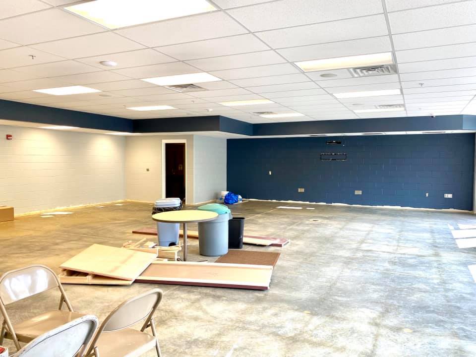 Empty office room with blue accent wall, tile ceiling, scattered furniture, and construction debris on the floor