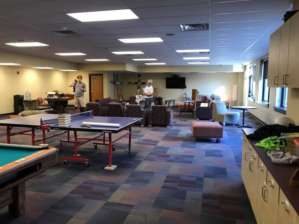 Spacious game room with ping-pong tables, couches, and overhead lights in a carpeted lounge area