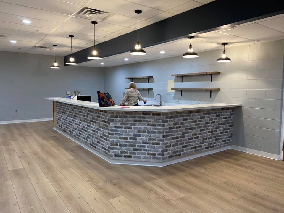 Modern empty café with white brick walls, curved brick counter, hanging lights, and wood flooring