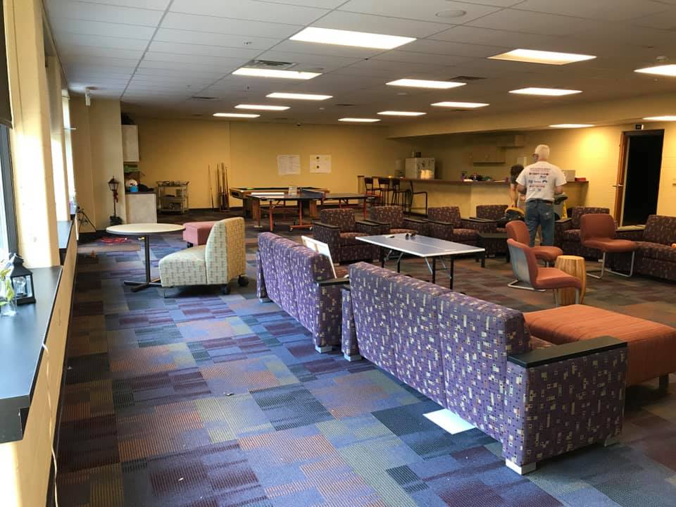 Spacious lounge with patterned couches, tables, and a person standing near the back wall