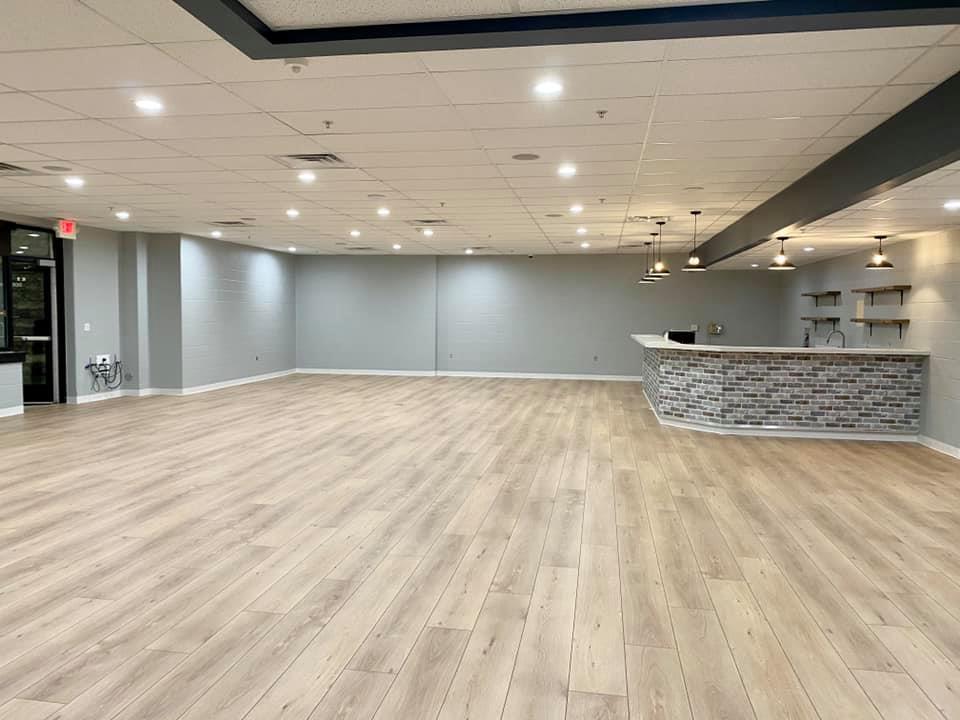 Empty modern lobby with light wood floors, gray walls, recessed lighting, and a stone-front reception counter