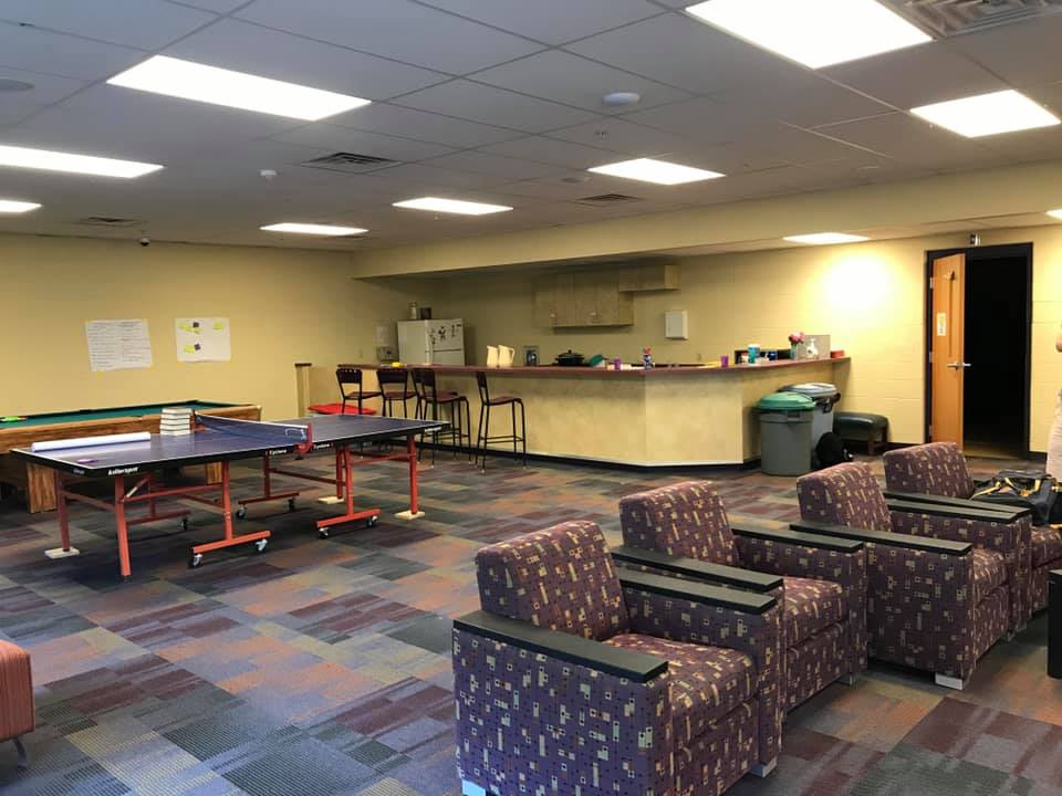 Spacious rec room with ping-pong table, patterned chairs, and a counter in the back.