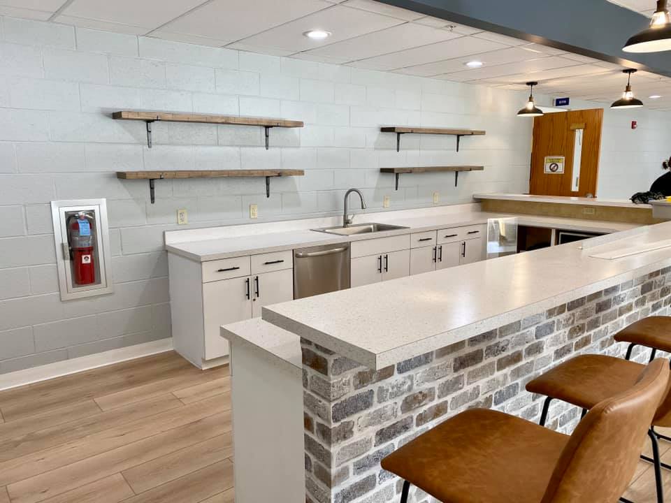 Bright, modern kitchen with white cabinets, open shelves, brick island, and two brown stools