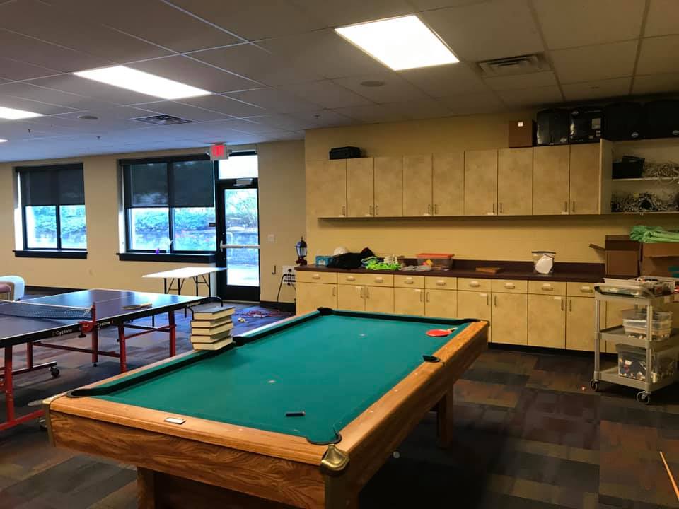 Recreation room with pool table, ping-pong tables, cabinets, and large windows.