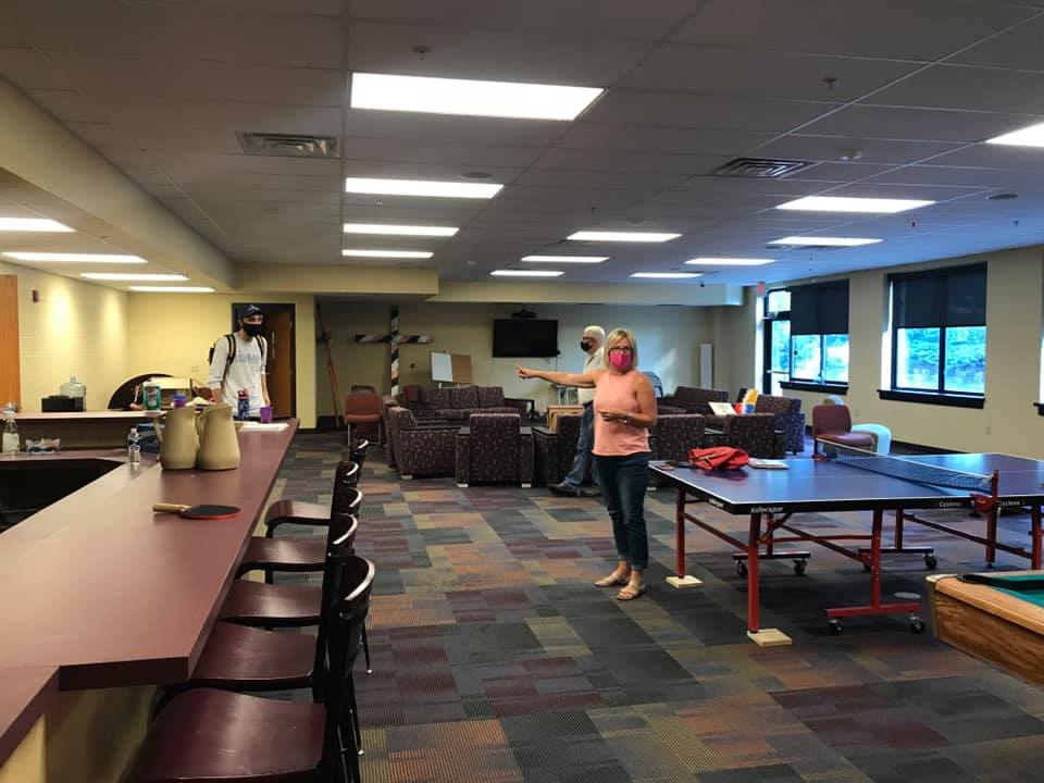 Recreation room with tables, chairs, and ping-pong tables; one person stands near the center.