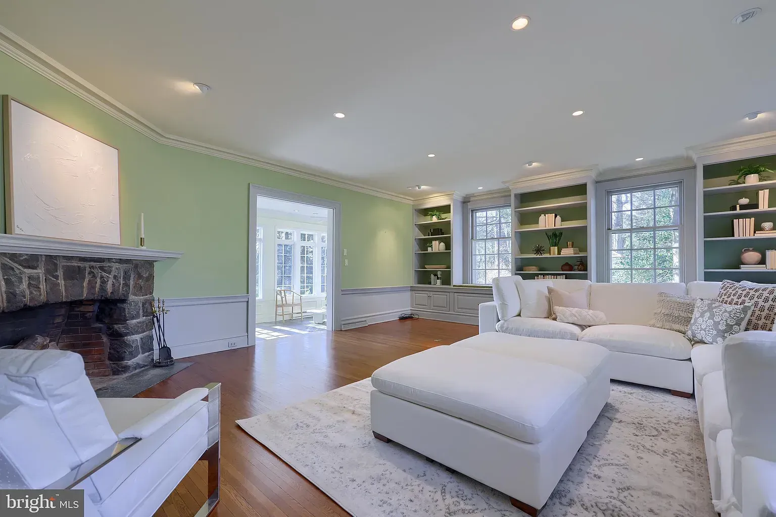 Bright living room with white sectional, stone fireplace, green walls, and large windows with built-in shelves