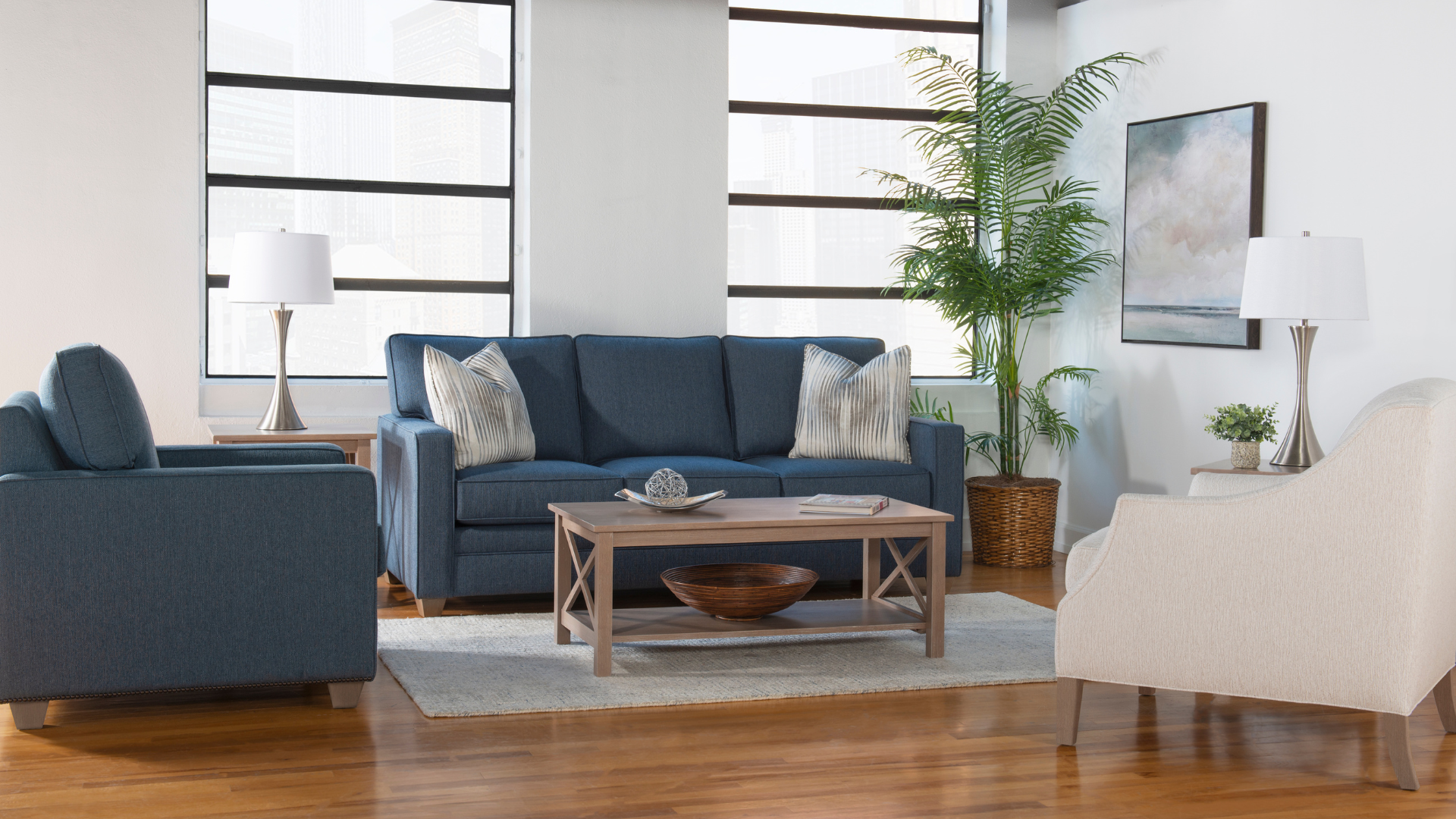 Modern living room with blue sofa, white armchair, wooden coffee table, and tall windows