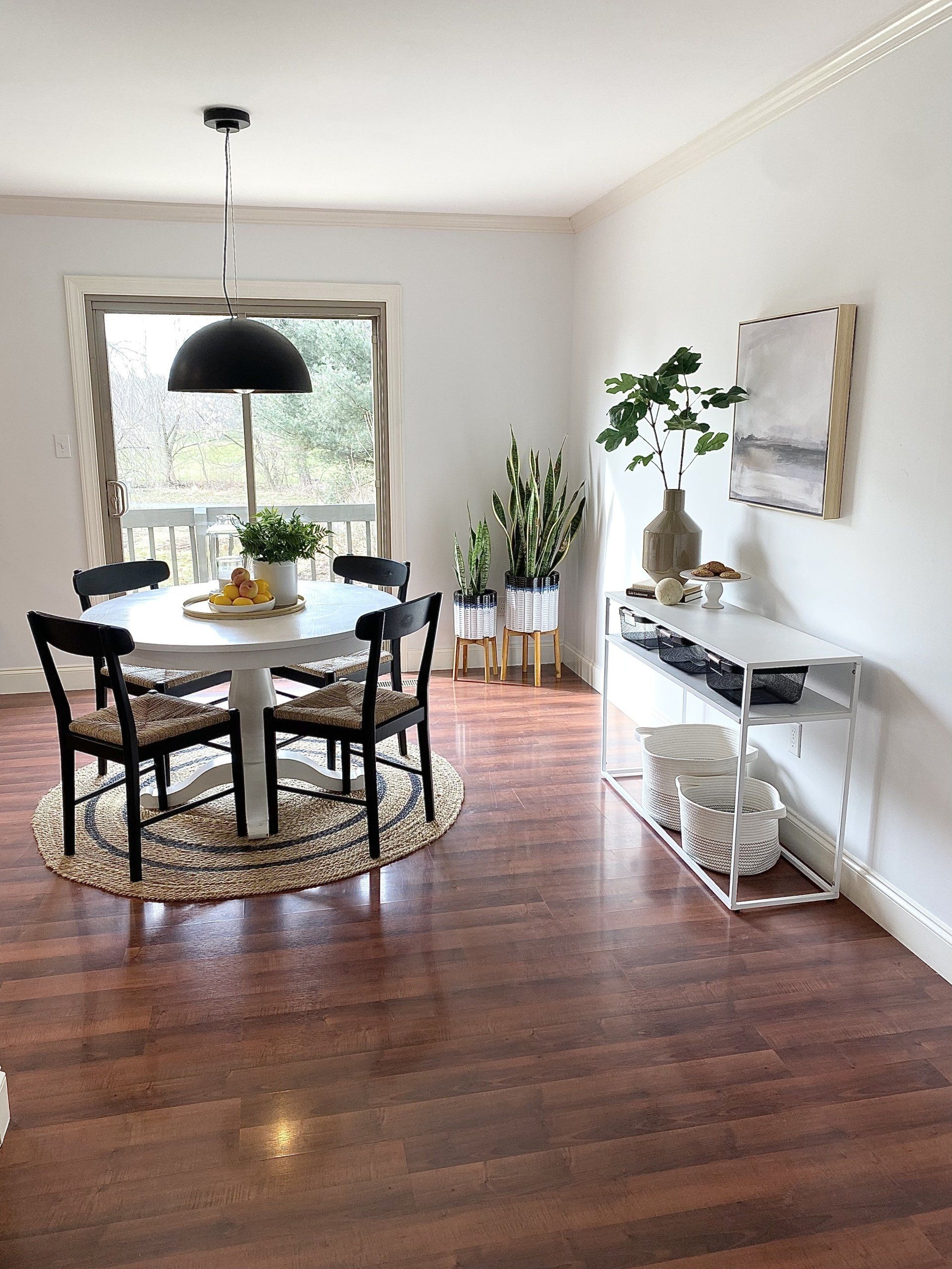 Bright dining room with round table, black chairs, hanging pendant light, plants, and wooden floors