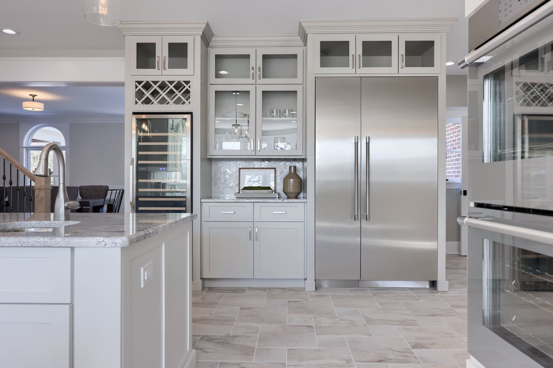 Bright modern kitchen with white cabinets, stainless steel fridge, and marble-look tile floor