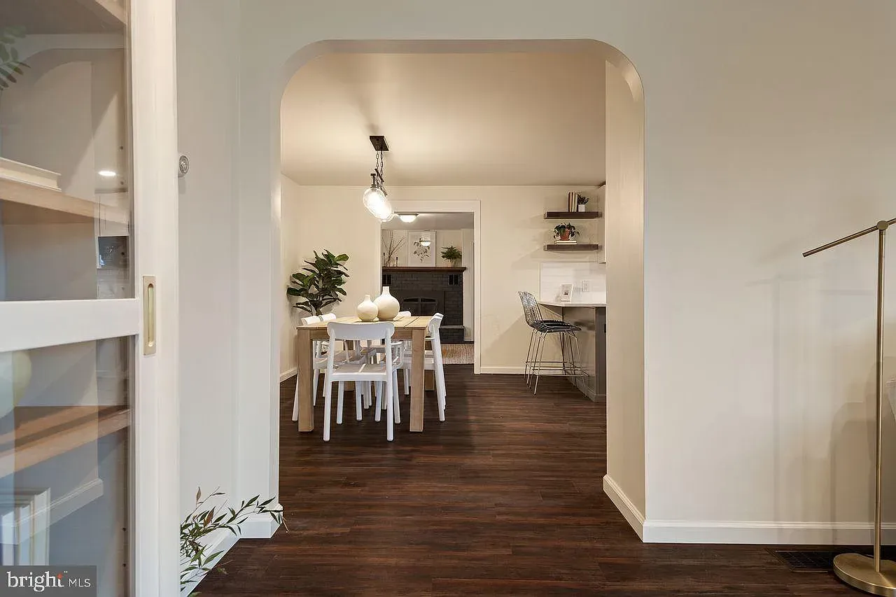 Bright dining room with white table, chairs, dark wood floors, and arched doorway to a kitchen area