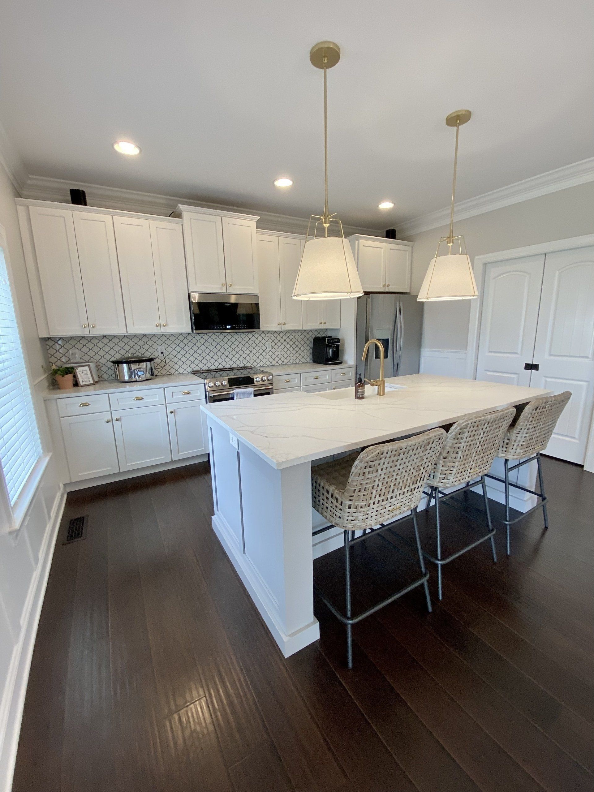 Bright kitchen with white cabinets, dark wood floors, island, and pendant lights
