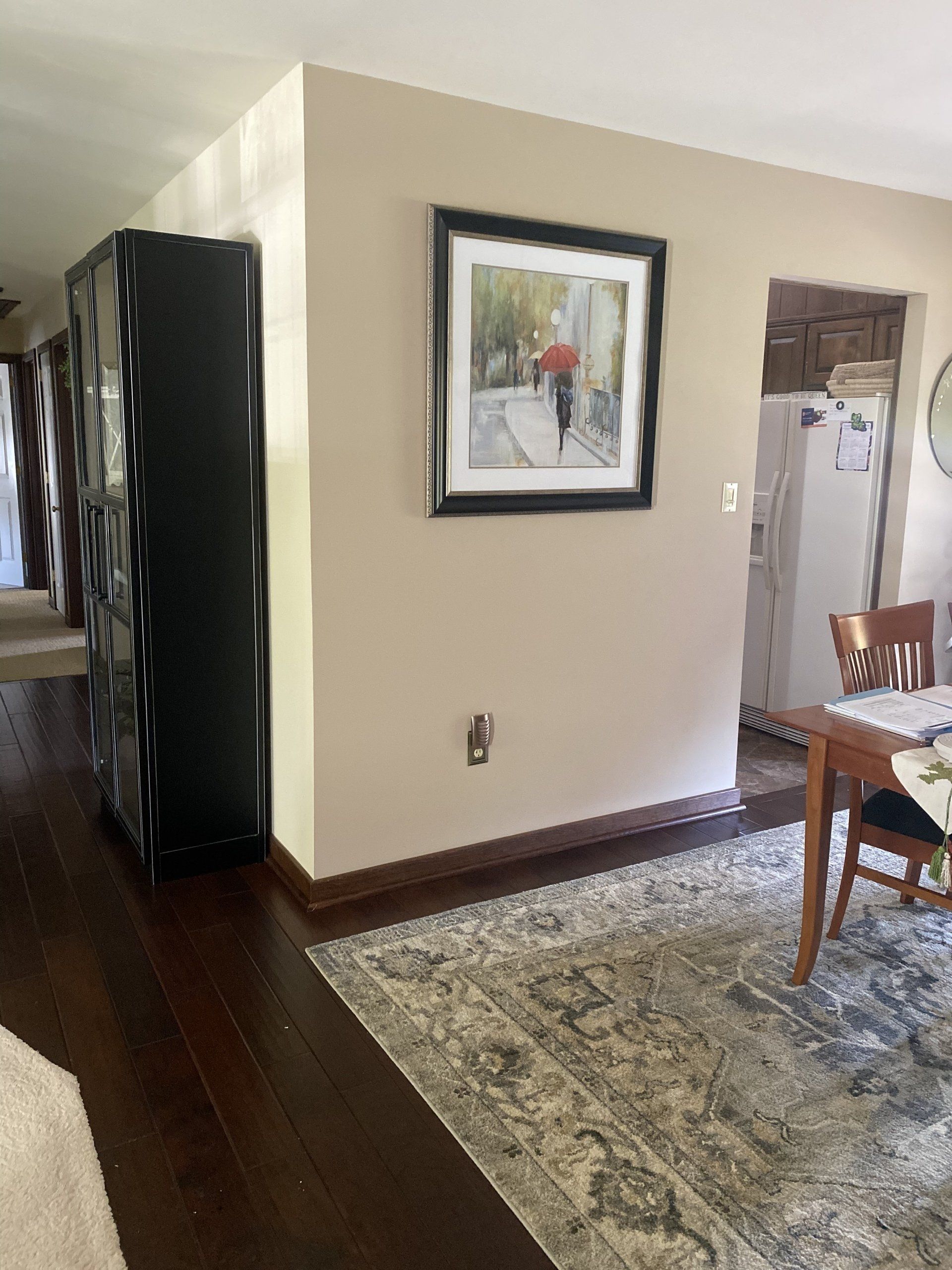Hallway with patterned rug, framed wall art, and dining table beside a kitchen doorway.