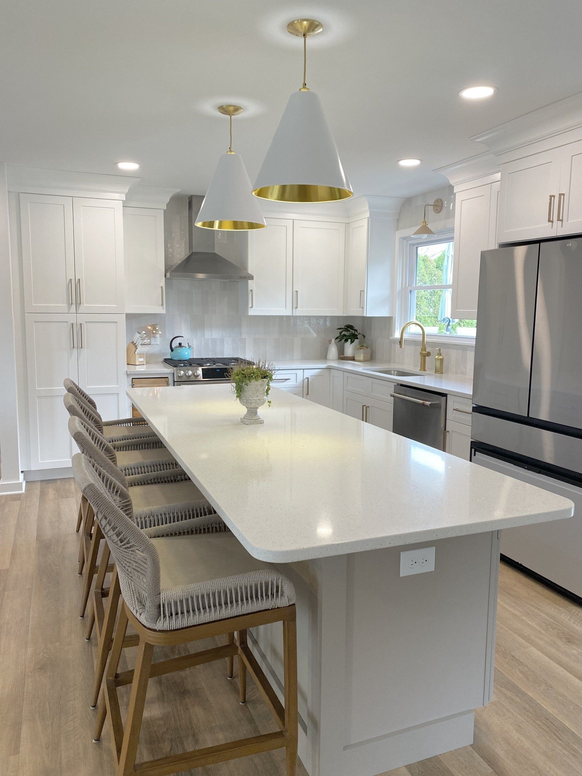 Bright modern white kitchen with large island, pendant lights, bar stools, and stainless steel appliances