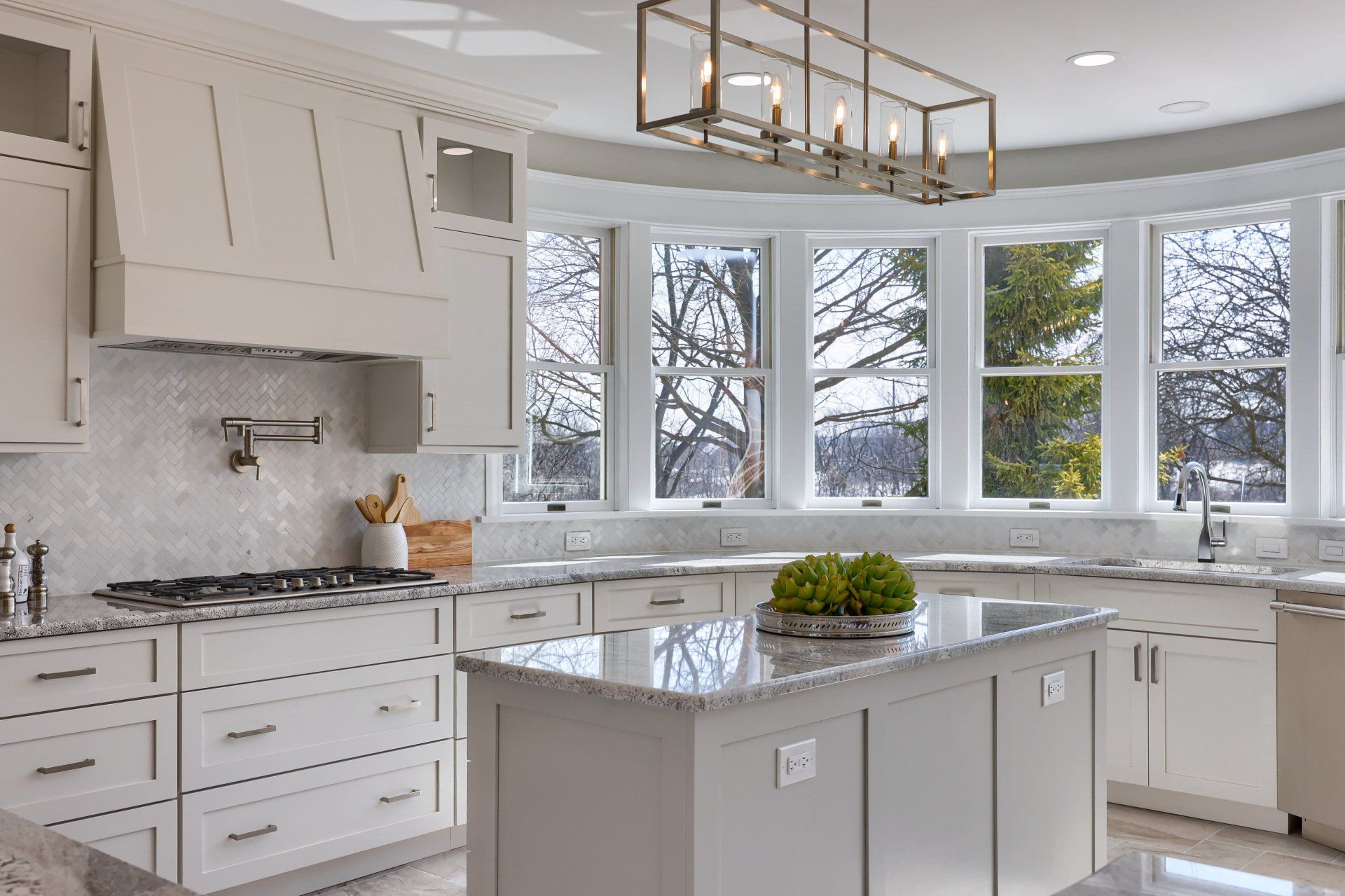 Bright white modern kitchen with marble island, pendant light, and large windows overlooking snowy trees