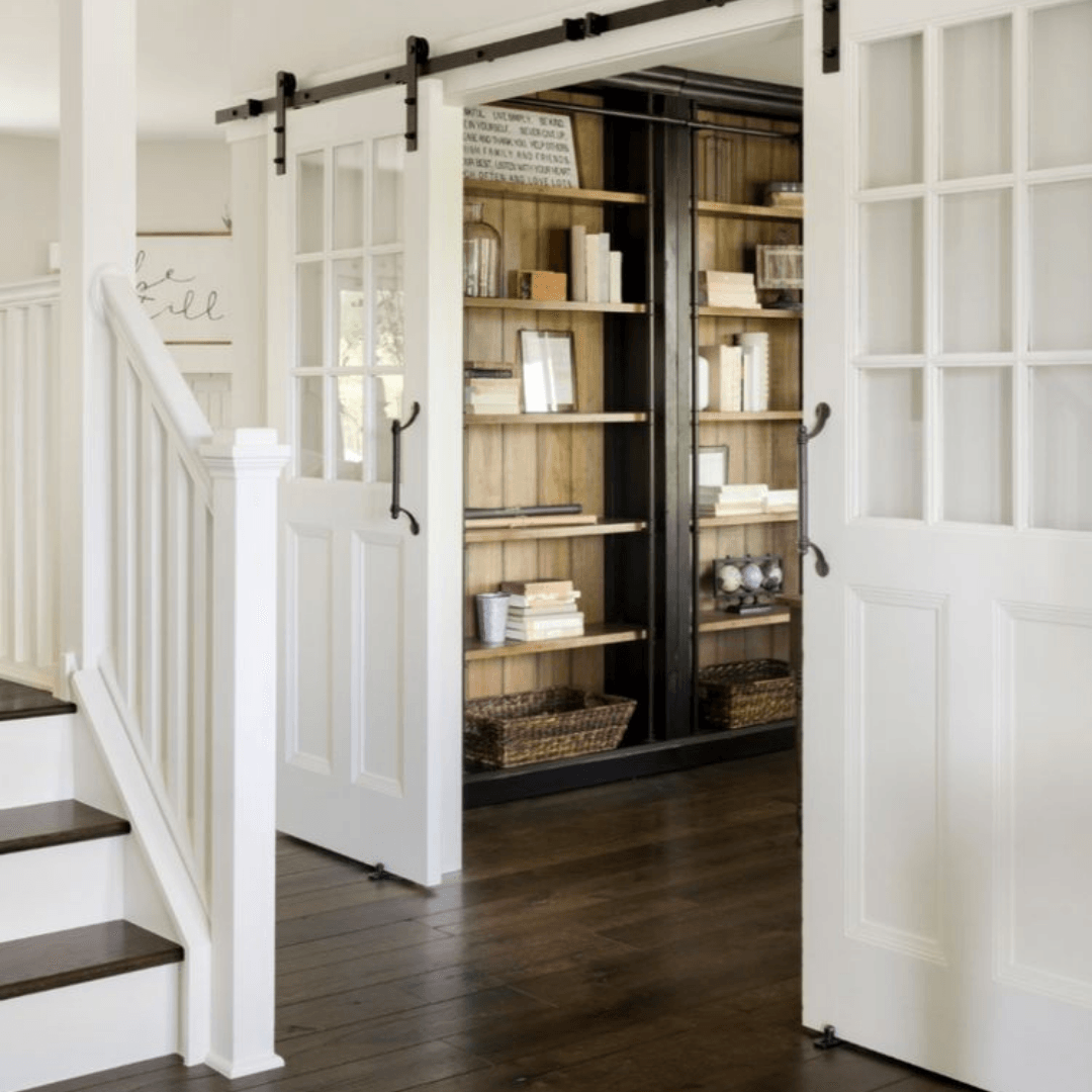 Bright hallway with open white doors revealing a dark wood bookshelf filled with books and baskets