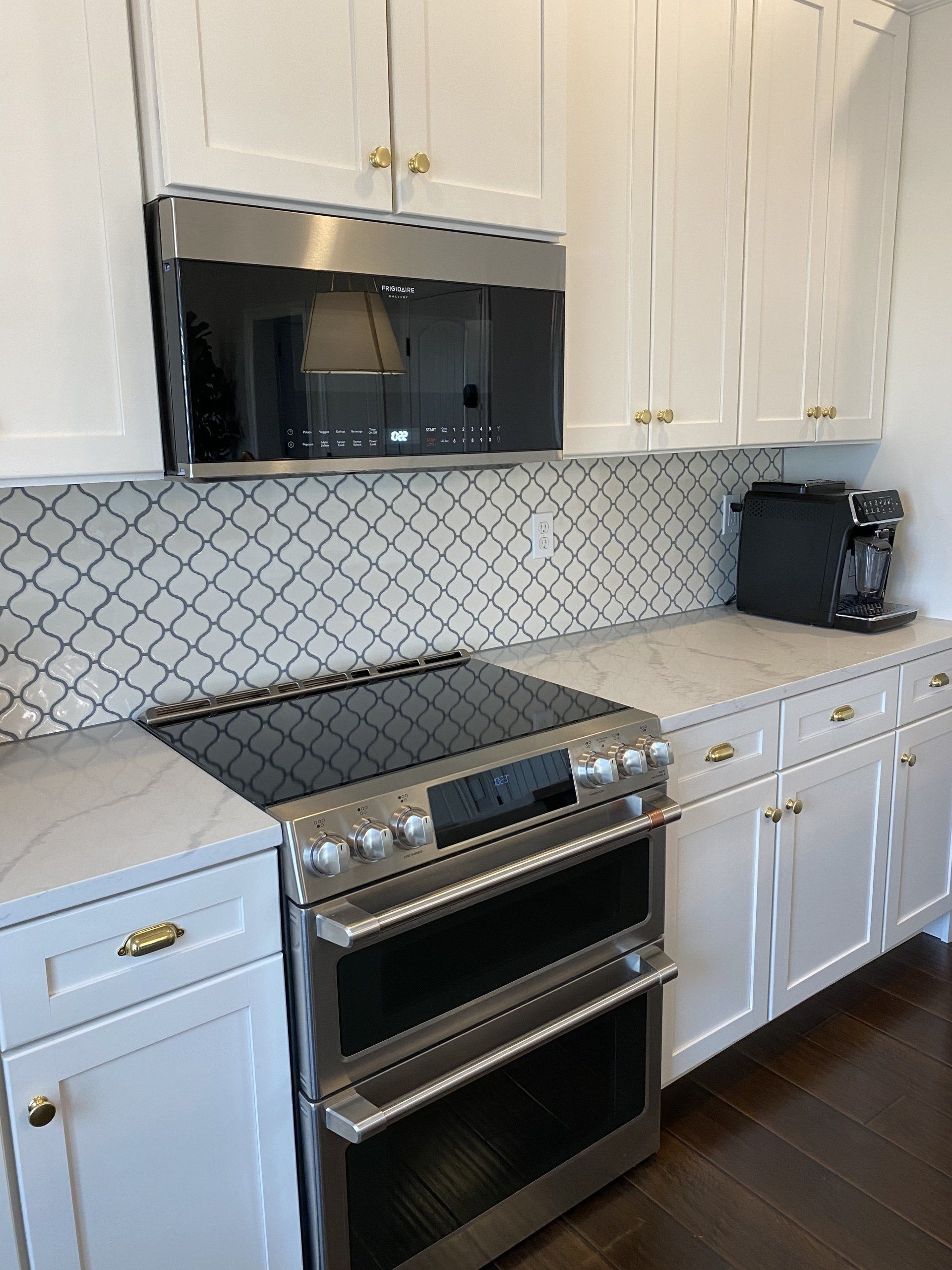 White kitchen with stainless steel range, white cabinets, patterned backsplash, and dark wood floor