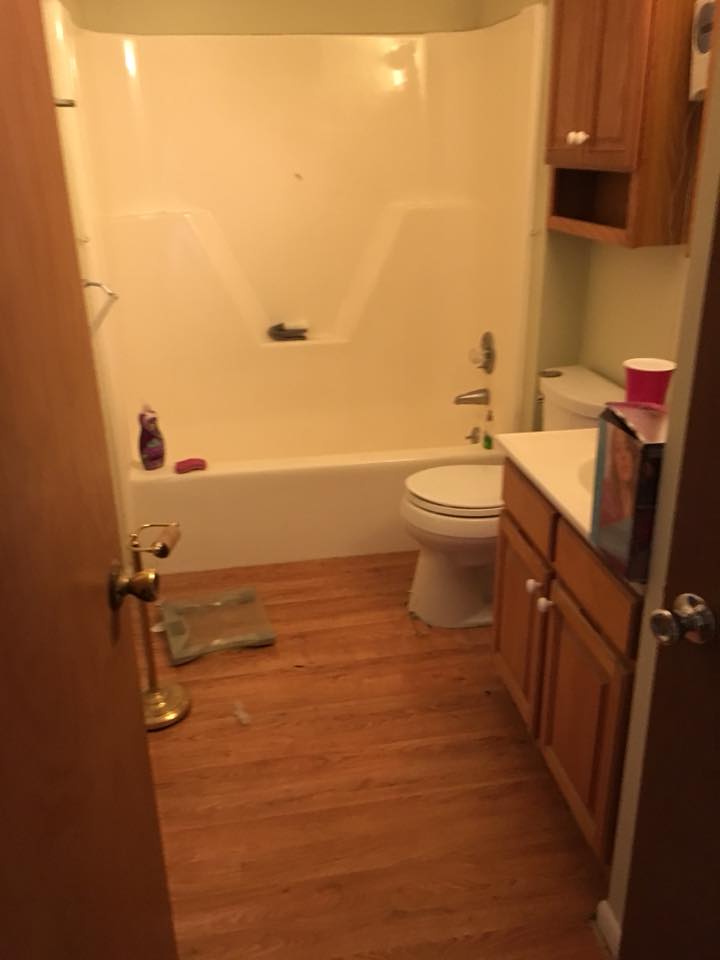 Small bathroom with a bathtub, toilet, wooden floor, and vanity cabinets.