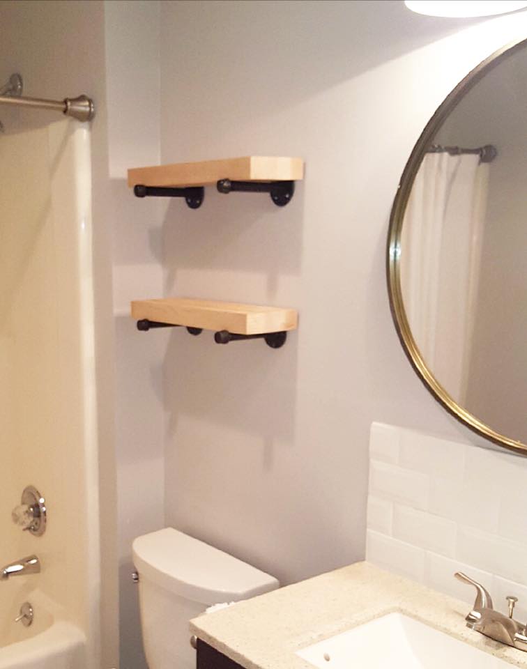 Bathroom with two wall shelves, a mirror, sink, toilet, and shower tub.
