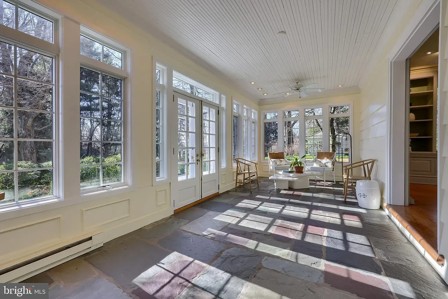 Sunlit empty room with large windows, white walls, and patterned carpet shadows