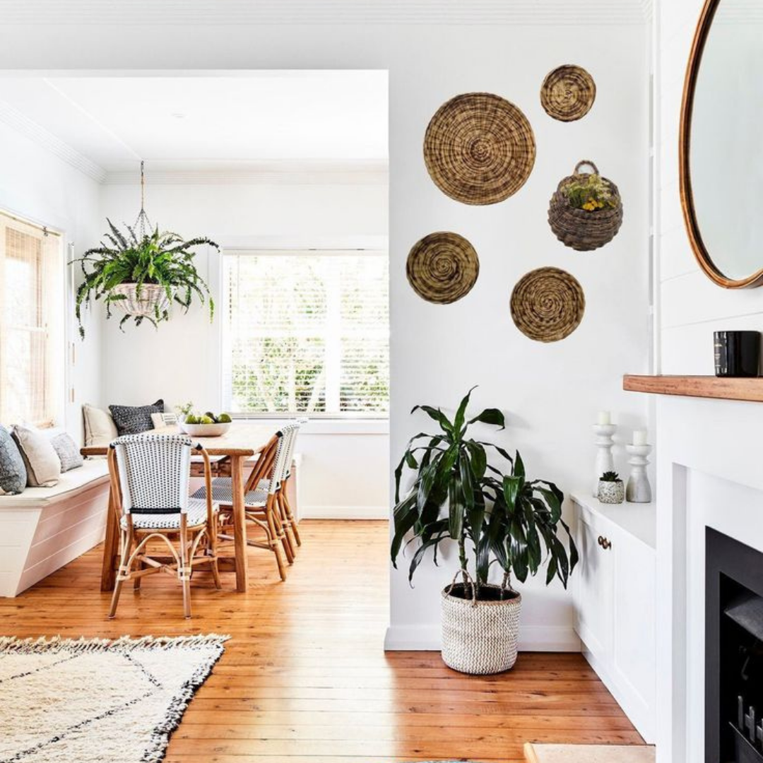 Bright dining room with wooden table, hanging plant, woven wall decor, and white fireplace in a sunlit home