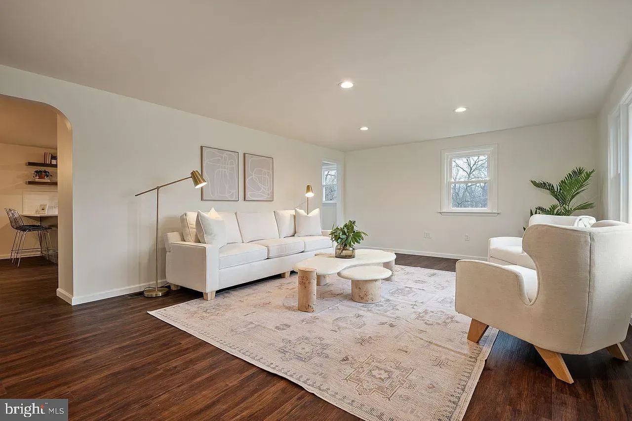 Bright modern living room with white sofas, beige rug, wood floors, and large windows
