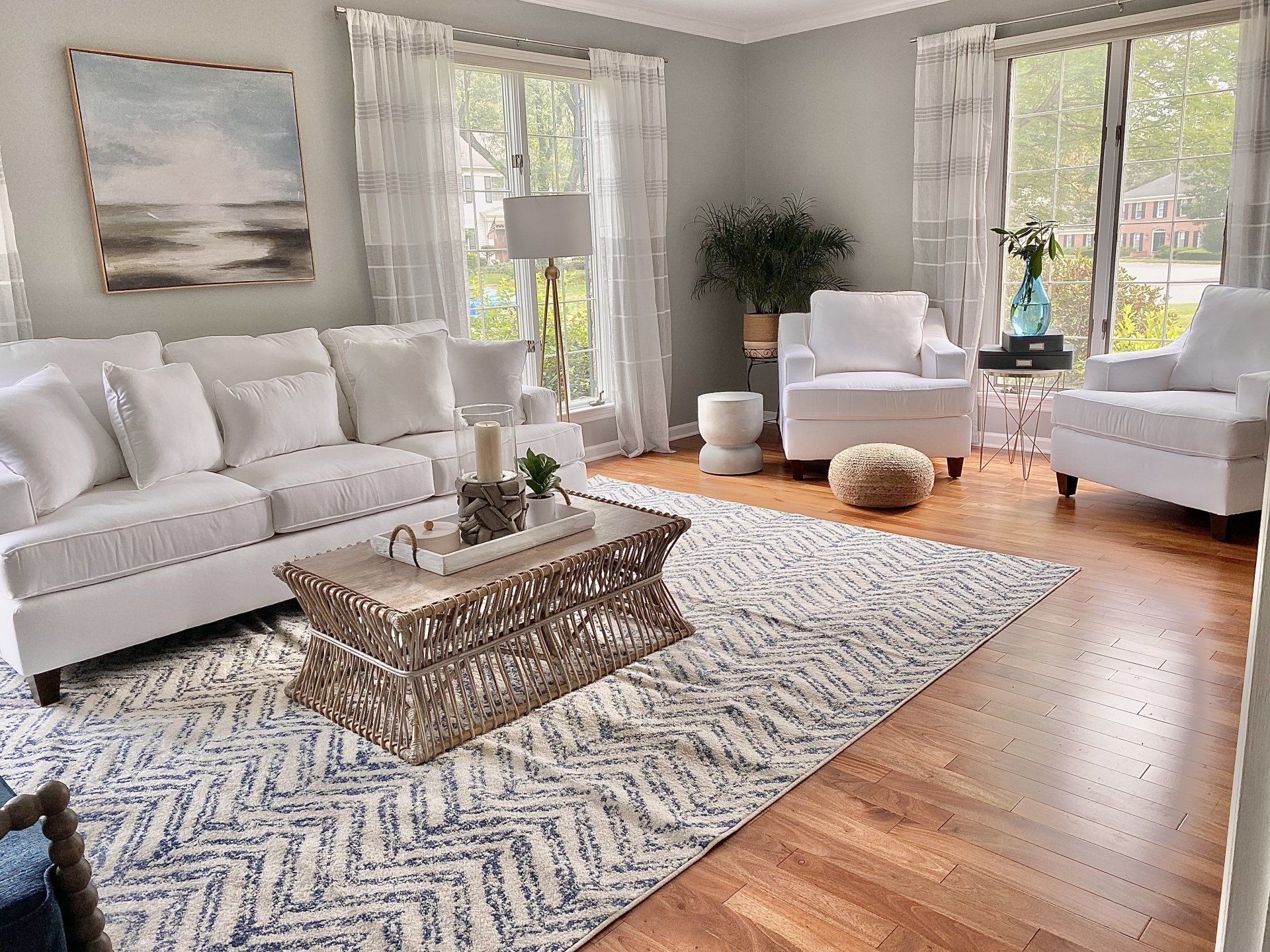 Bright living room with white sofa, patterned rug, coffee table, and large windows on hardwood floors