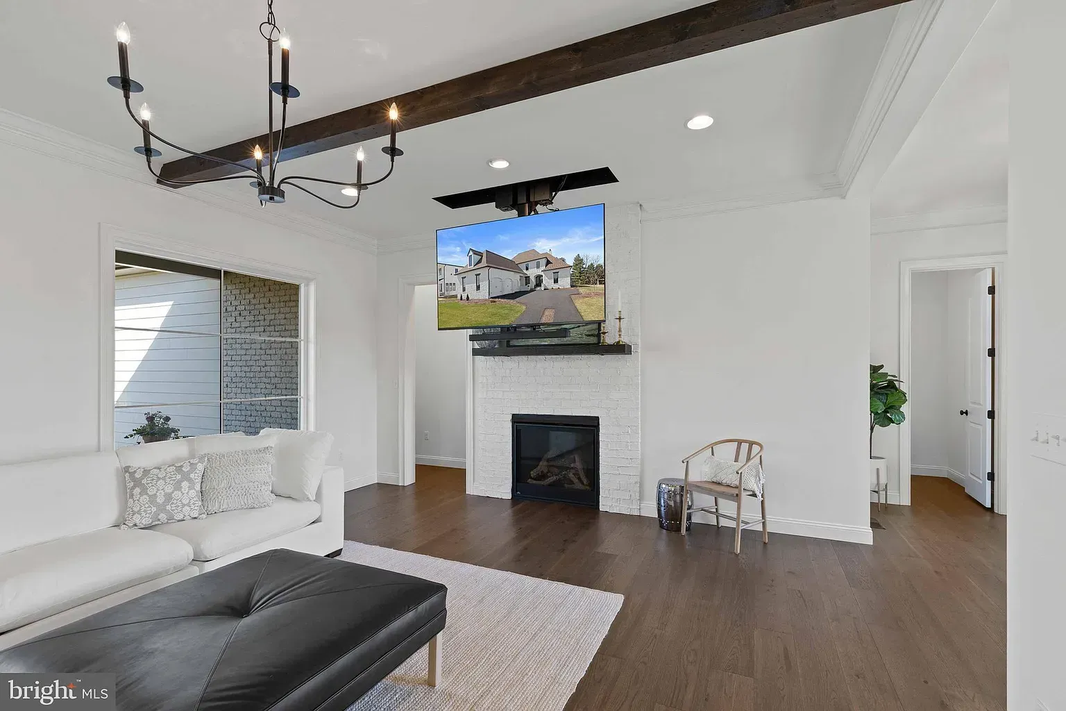Bright living room with white walls, dark wood floors, fireplace, chandelier, and wall-mounted TV